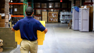A mover from RCS Moving & Storage carries yellow moving bins through a warehouse in Richmond, VA.