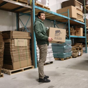 A Mastodon Moving LLC mover carrying a branded box in a warehouse facility in Westborough, MA.