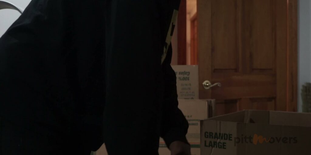 A mover carrying a box inside a home, with a PittMovers branded box in the foreground in McKees Rocks, PA