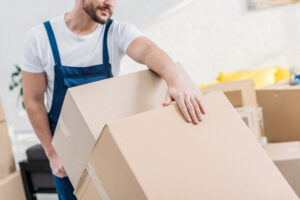A professional mover from Three Movers in Henderson, NV, carrying two cardboard boxes.