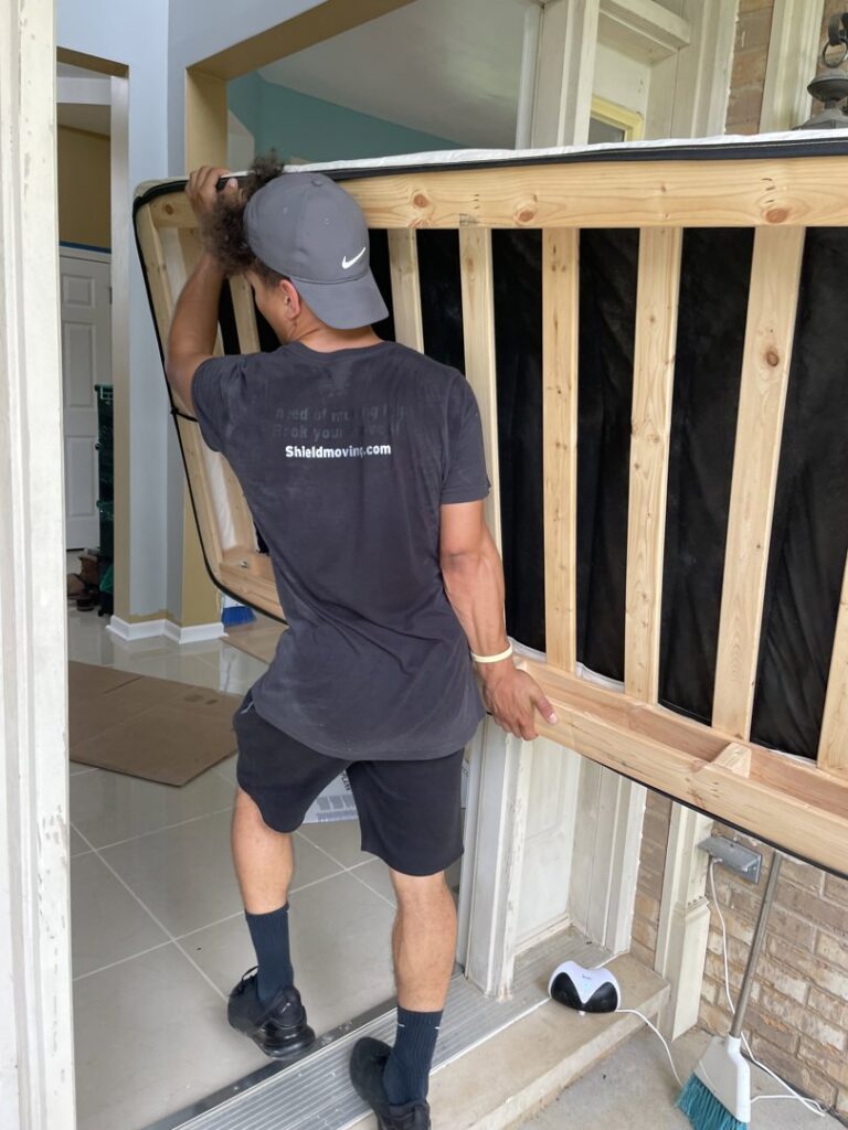 A Shield Moving Services mover carrying a mattress frame through a doorway in Milwaukee, WI.