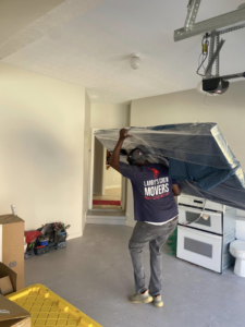 A mover from Larry's Crew Movers in Atlanta, GA, carrying a wrapped mattress into a garage.