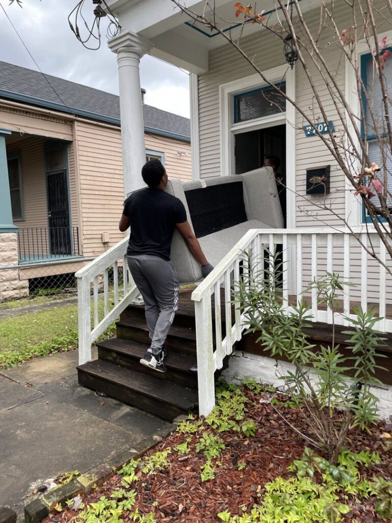A mover carefully carrying a sofa into a house for ASAP Elite Hauling and Delivery in New Orleans, LA.