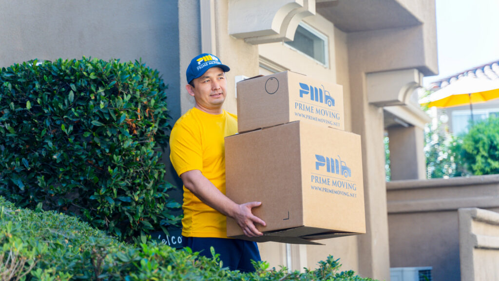 A Prime Moving professional carrying three branded moving boxes in Boston, MA.