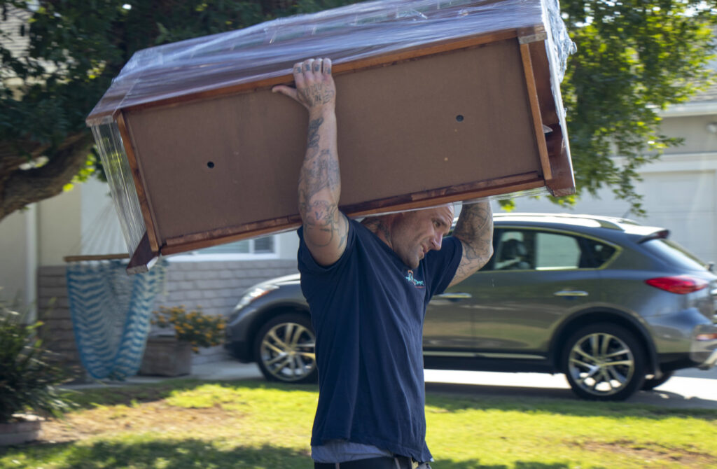A mover from Cheap Movers Los Angeles carrying a plastic-wrapped dresser on his shoulders in Los Angeles, CA.