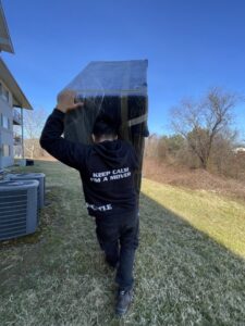 A J.Gentle Van Lines mover carrying a large, wrapped item on his back across a grassy area in Elizabeth, NJ.