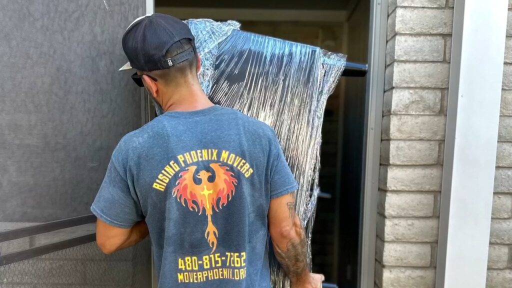 A mover from Rising Phoenix Movers LLC carrying a carefully wrapped item through a doorway in Phoenix, AZ.