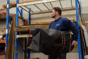 A mover from N. L. Wilson Moving and Storage carrying a blanket-wrapped item in a warehouse in Olathe, KS.