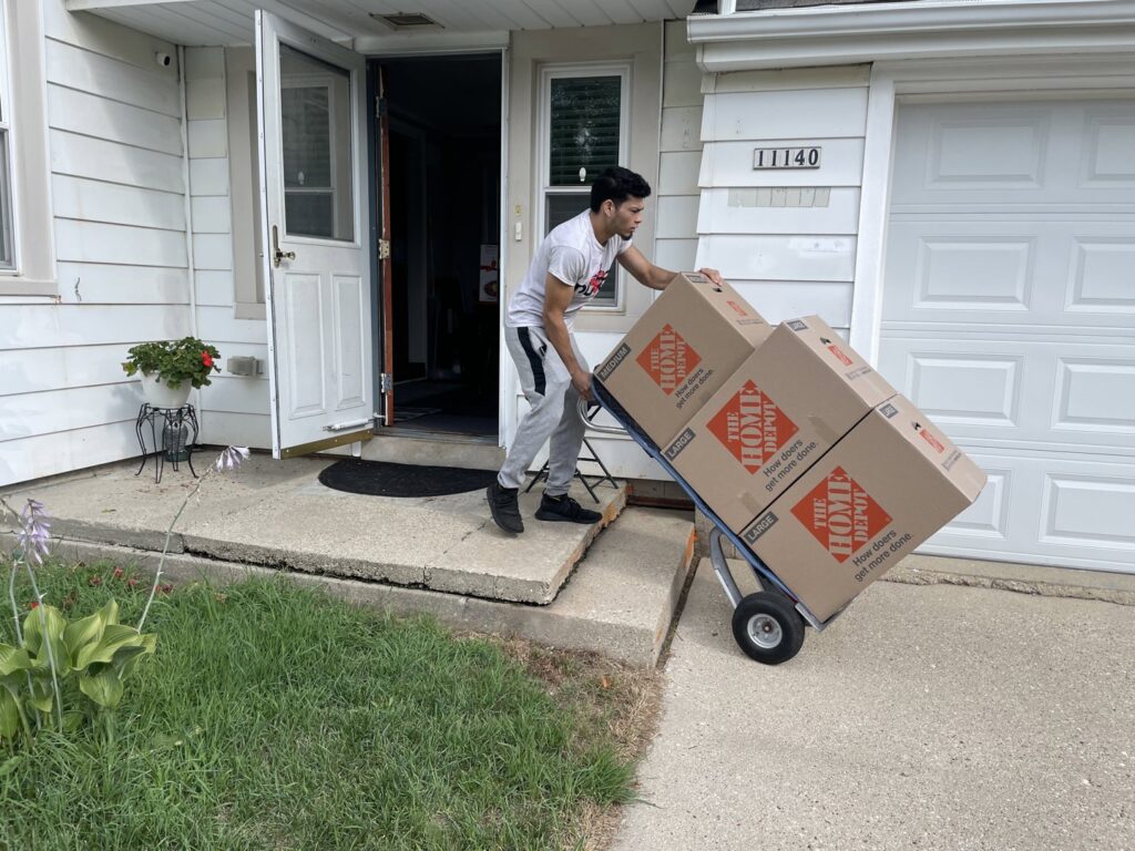 A Shield Moving Services mover delivering moving boxes on a hand truck to a residence in Milwaukee, WI.