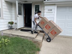 A Shield Moving Services mover delivering moving boxes on a hand truck to a residence in Milwaukee, WI.