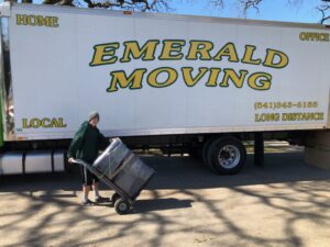 A mover from Emerald Moving & Storage, Inc. uses a dolly to load items onto a moving truck in Eugene, OR.