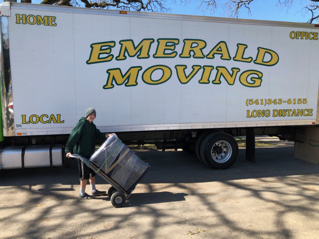 A mover from Emerald Moving & Storage, Inc. uses a dolly to load items onto a moving truck in Eugene, OR.