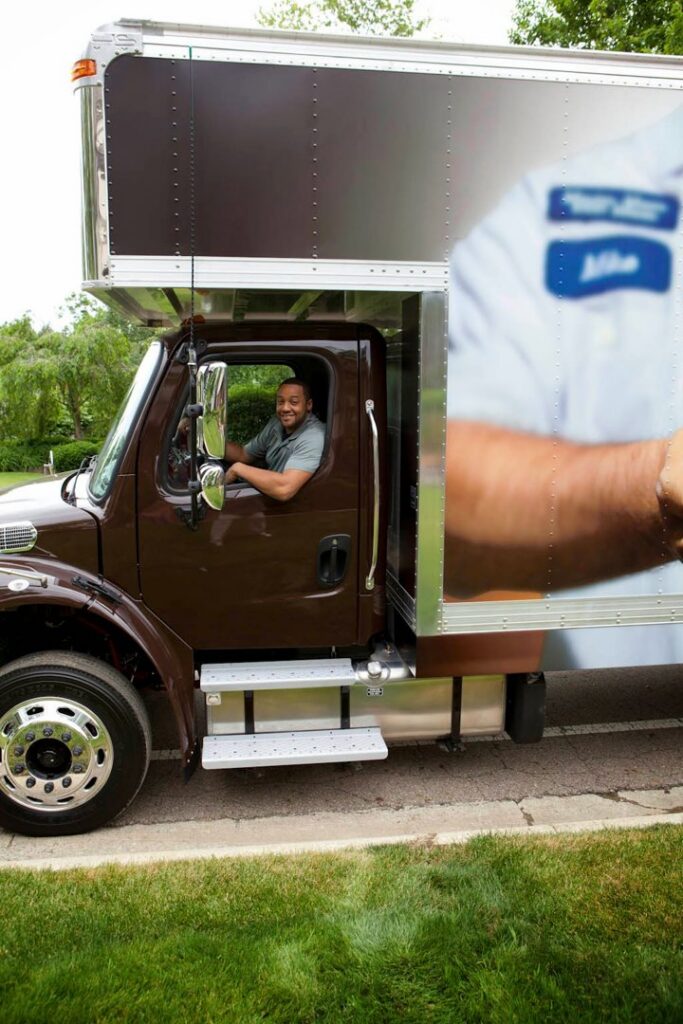 A smiling mover from Leaders Moving & Storage Co. driving a branded moving truck in Indianapolis, IN.