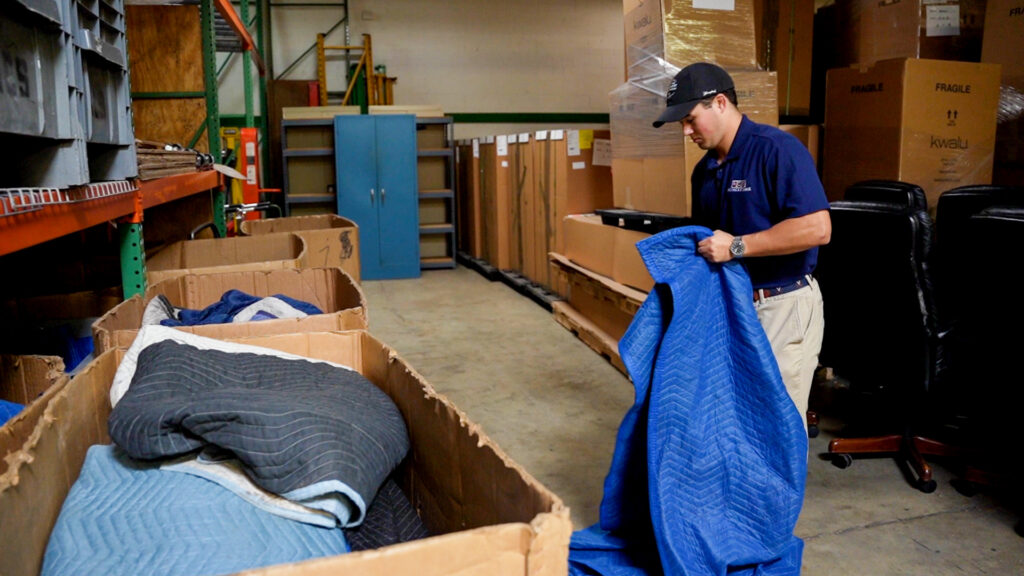 A mover from RCS Moving & Storage folds a protective moving blanket in a warehouse, preparing for a job in Richmond, VA.