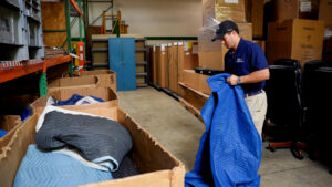 A mover from RCS Moving & Storage folds a protective moving blanket in a warehouse, preparing for a job in Richmond, VA.