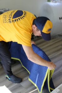 A mover from Sunshine Moving Services LLC carefully folding a blue moving blanket in San Diego, CA.