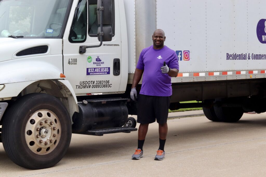 A friendly mover from Kingdom Men Movers in Houston, TX, giving a thumbs up next to a large moving truck.