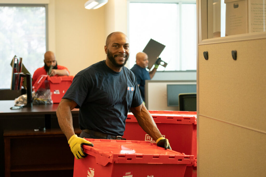 A friendly mover from RCS Moving & Storage handles red moving bins inside an office during a commercial relocation in Richmond, VA.