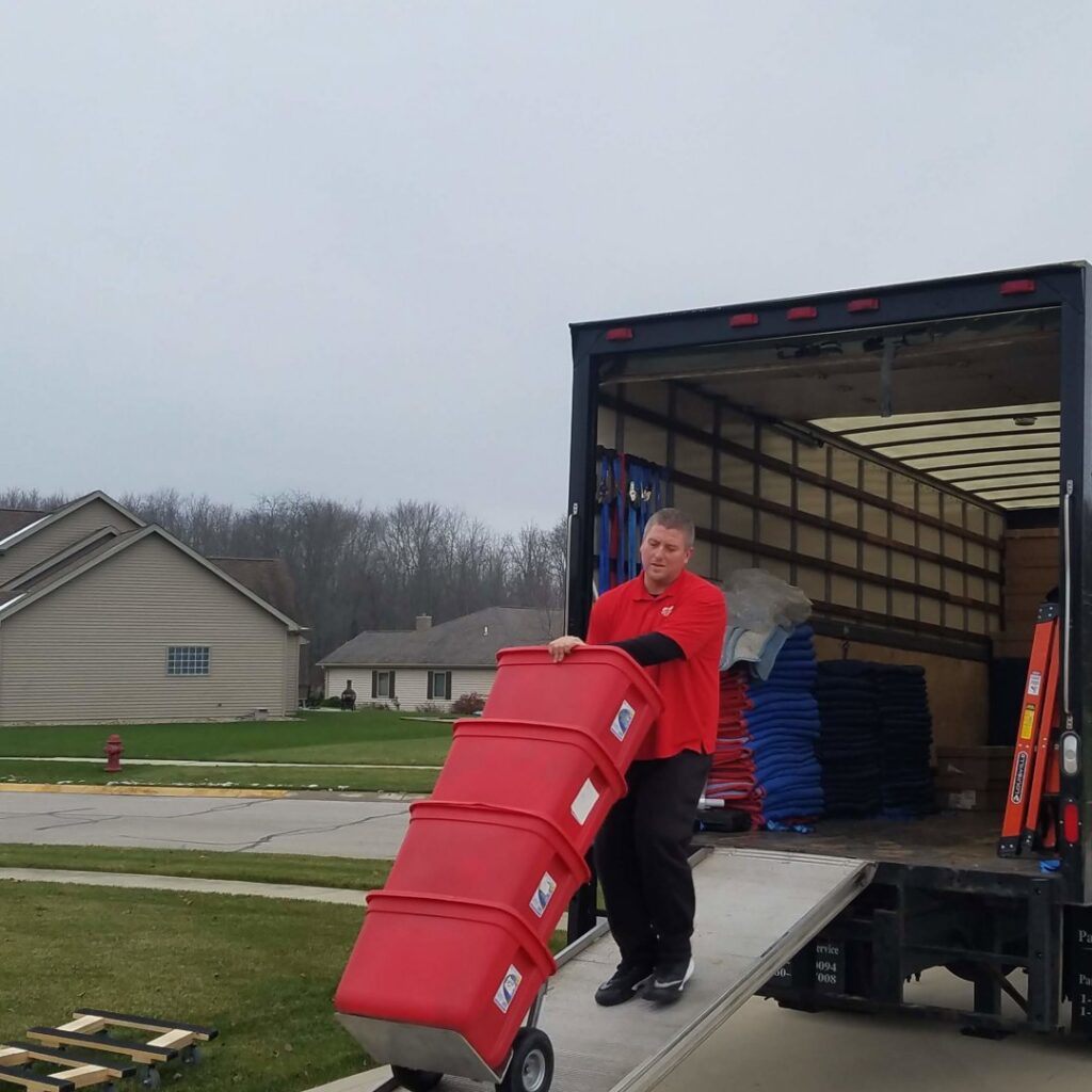 A professional mover from Joy Haul Professional Movers loading a large red bin onto a truck using a ramp in Columbia City, IN.