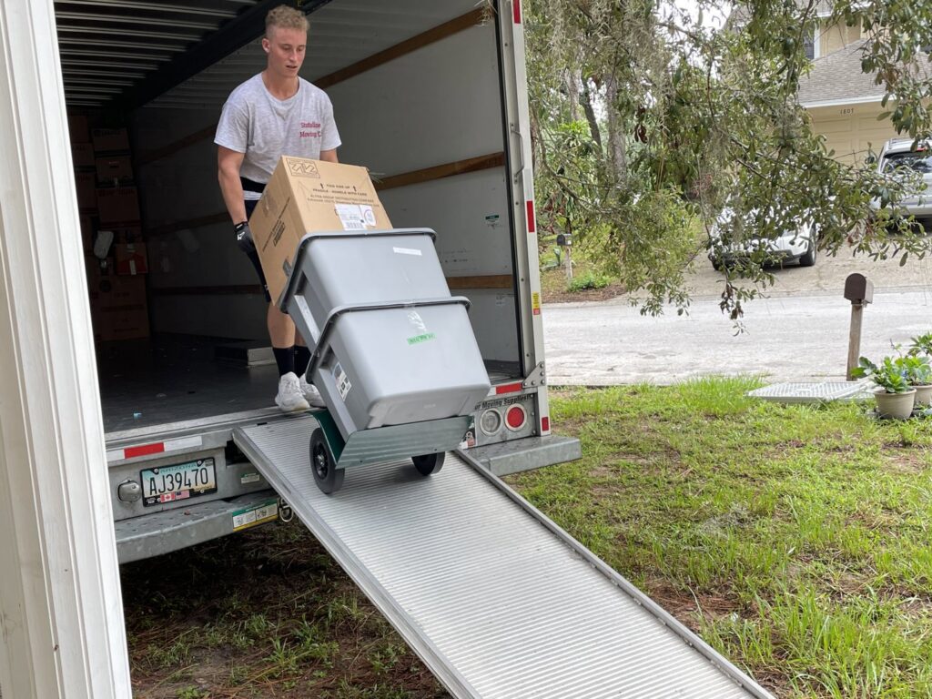 A mover from The Local Movers loading moving boxes with a hand truck up a ramp into a moving truck in Orlando, FL.