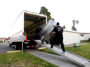 A Packman Moving professional loading a large, wrapped item onto a truck using a dolly in San Diego, CA