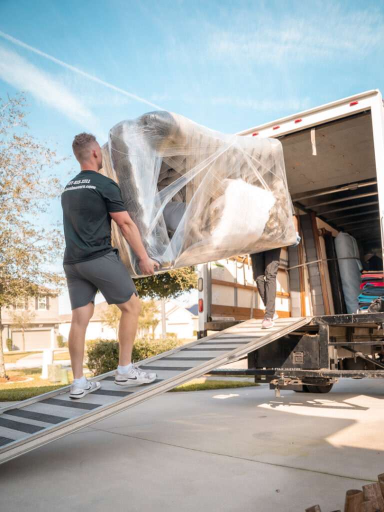 A mover from The Local Movers loading a large, wrapped furniture item onto a moving truck in Orlando, FL.