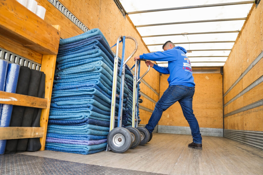 A mover loading a stack of blue moving blankets onto a dolly inside a truck for Let's Get Moving in Saint Petersburg, FL.