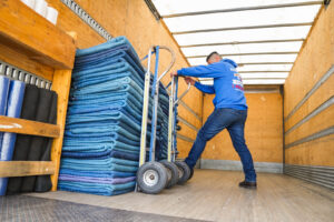 A mover loading a stack of blue moving blankets onto a dolly inside a truck for Let's Get Moving in Saint Petersburg, FL.