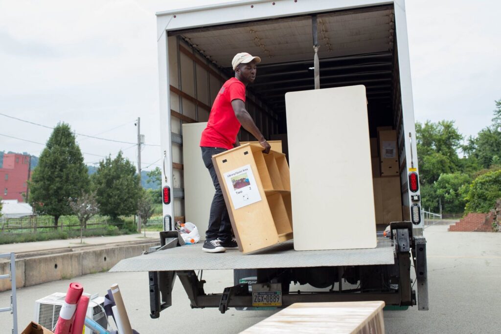 A PittMovers team member loading a wooden shelf onto a moving truck using a ramp in McKees Rocks, PA