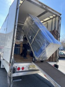 A J.Gentle Van Lines mover pushes a large, wrapped item on a dolly up a ramp into a moving truck in Elizabeth, NJ.