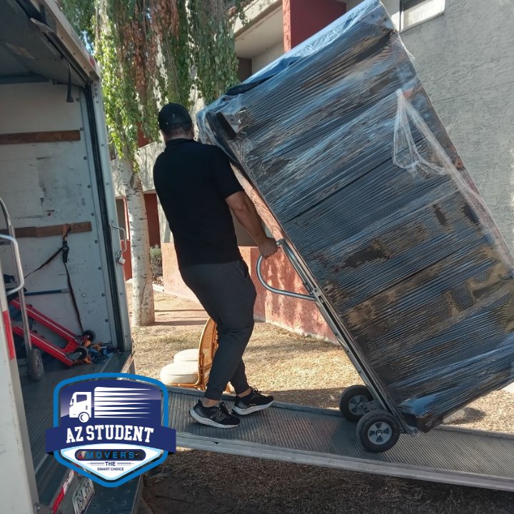 A professional mover loading a large, wrapped piece of furniture onto a moving truck using a ramp for Az Student Movers in Scottsdale, AZ
