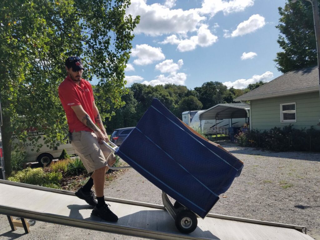 A professional mover from Joy Haul Professional Movers loading a large, wrapped item onto a truck via a ramp in Columbia City, IN.