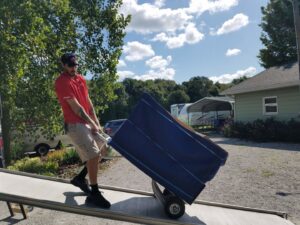 A professional mover from Joy Haul Professional Movers loading a large, wrapped item onto a truck via a ramp in Columbia City, IN.