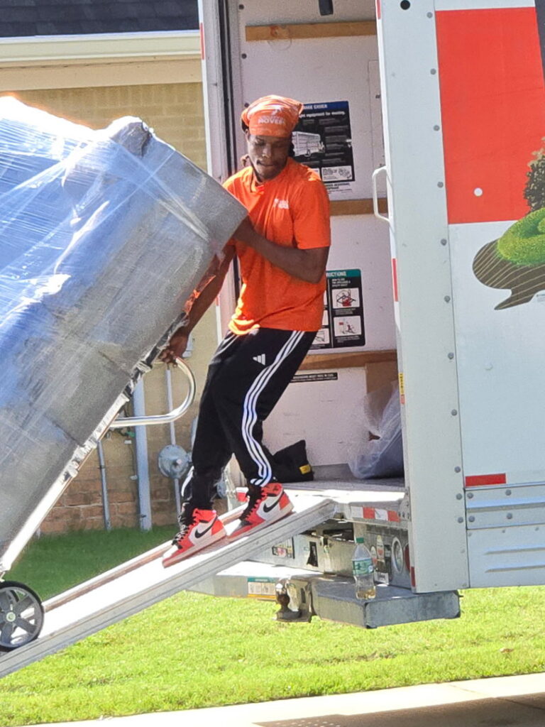 A Jubilee City Movers team member loading a large, wrapped item onto a moving truck using a ramp in Montgomery, AL.
