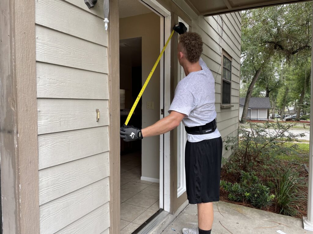 A mover from The Local Movers measuring a doorway with a tape measure to ensure furniture clearance in Orlando, FL.