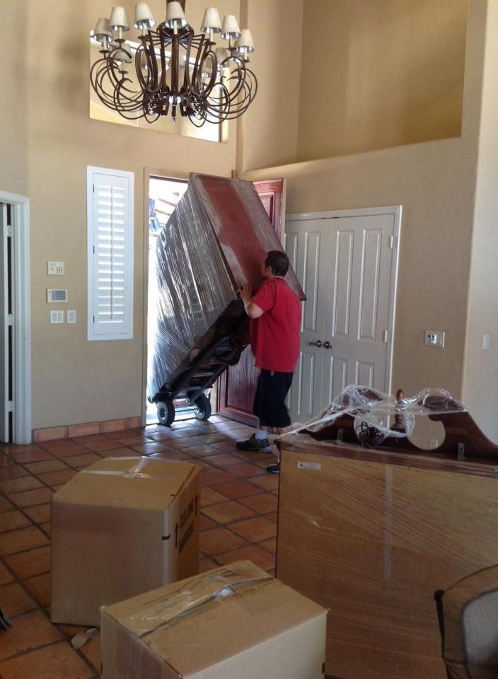 A professional mover using a dolly to move wrapped furniture for First Class Moving & Storage in Phoenix, AZ
