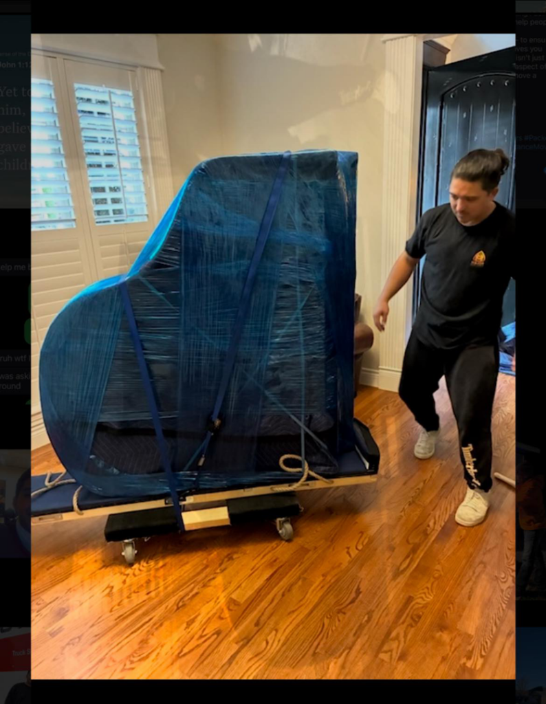 A professional mover from Major Movers LLC carefully transporting a wrapped piano on a dolly inside a home in Bentonville, AR.