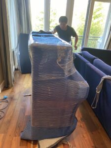 A mover moving a large, wrapped piece of furniture on a dolly inside a home for IMoving Professional Moving System Inc. in San Francisco, CA