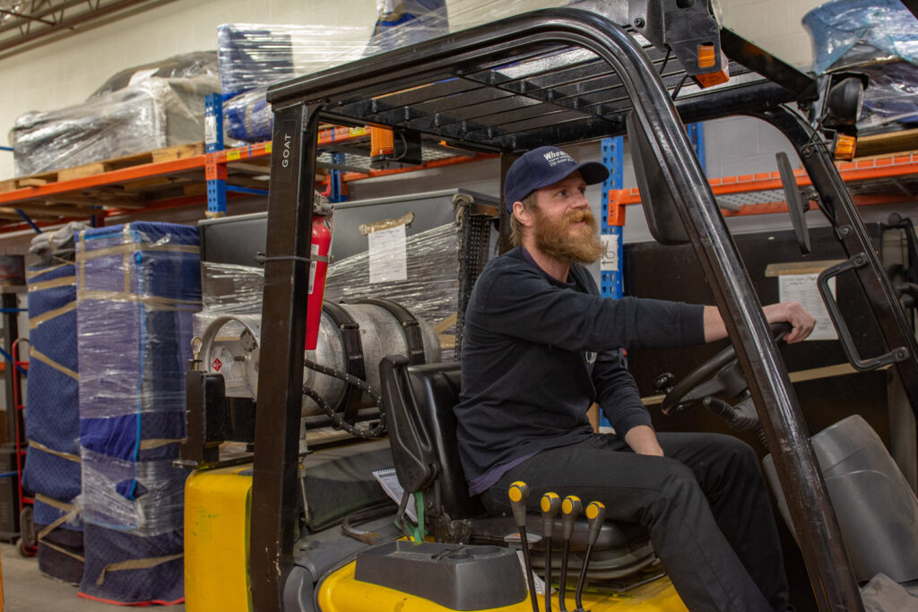 A mover from N. L. Wilson Moving and Storage operating a forklift in a warehouse with stored items in Olathe, KS.
