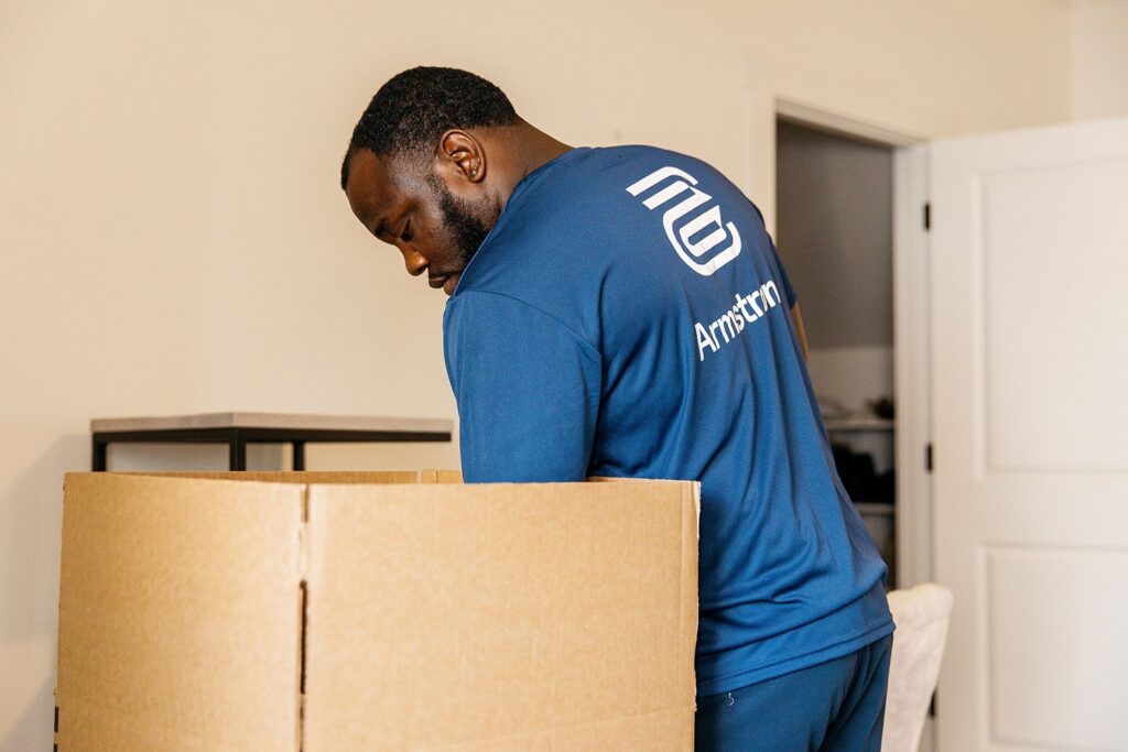 A mover from The Armstrong Company packing items into a large cardboard box inside a home in Huntsville, AL.