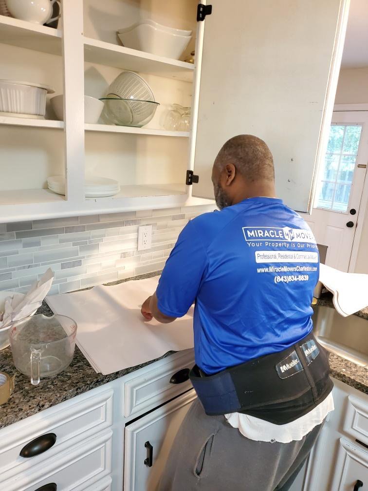 A professional mover from Miracle Movers of Charleston, SC carefully packing dishes in a kitchen as part of a moving service in Summerville, SC.