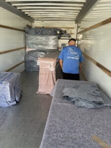 A mover from Reynolds Moving in Baton Rouge, LA, standing inside a truck with wrapped furniture and moving blankets