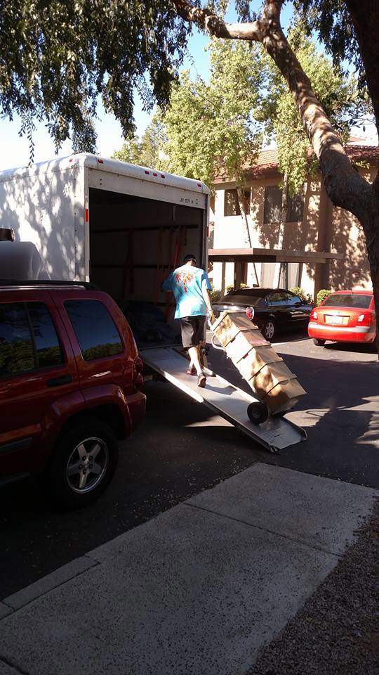 A mover from Rising Phoenix Movers LLC pushing a stack of boxes on a dolly up a ramp into a moving truck in Phoenix, AZ.