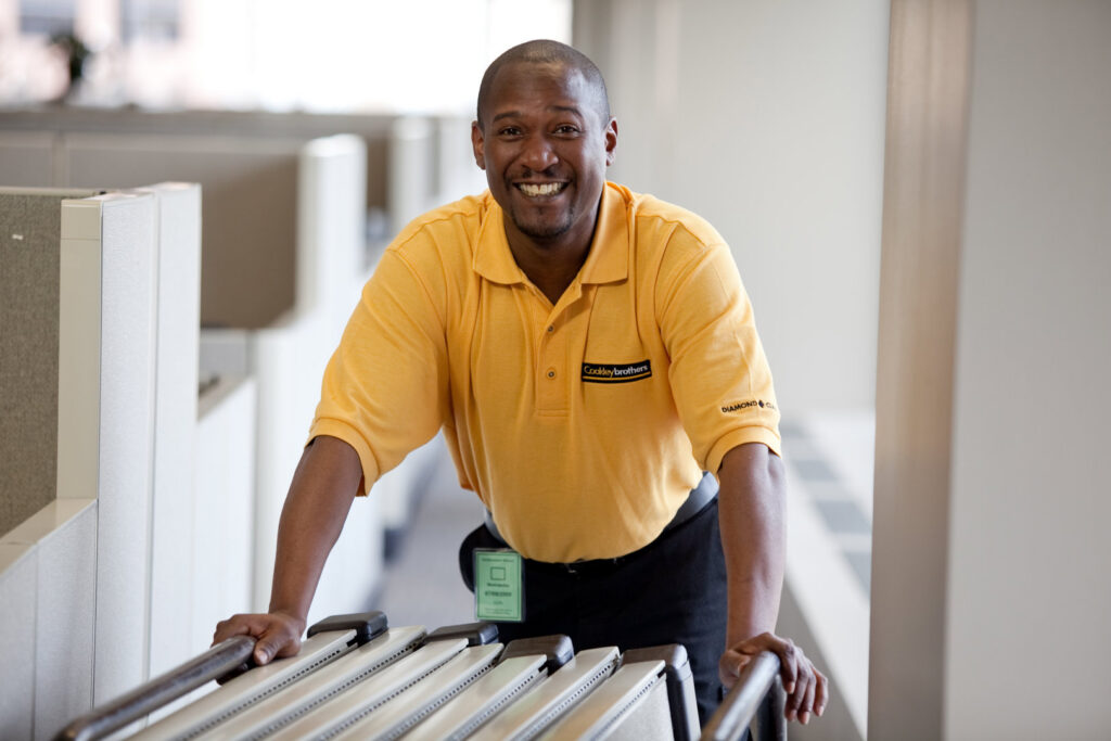 A smiling mover in a Coakley Brothers shirt pushing a cart in an office for Coakley Brothers & Brothers Interiors in Milwaukee, WI.