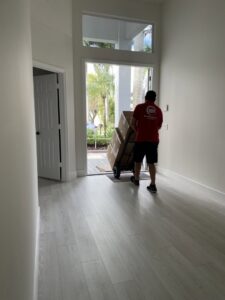 A professional mover from Orellana AV Moving in Miami, FL, pushing a dolly with packed boxes towards the entrance of a house.