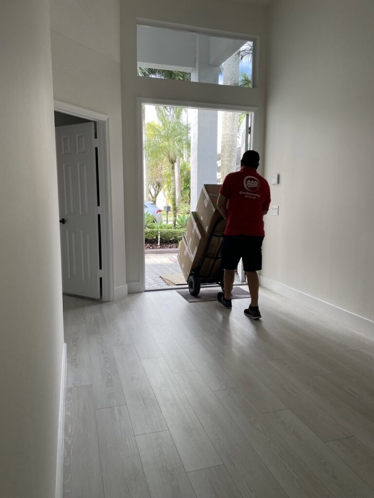 A professional mover from Orellana AV Moving in Miami, FL, pushing a dolly with packed boxes towards the entrance of a house.