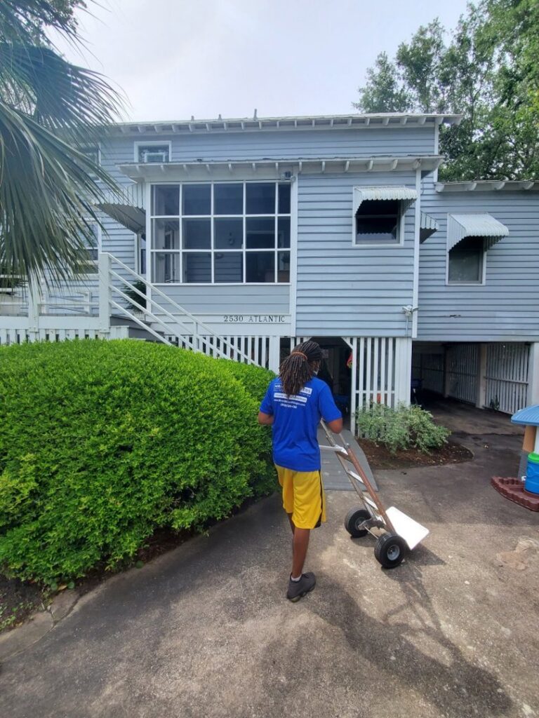 A professional mover from Miracle Movers of Charleston, SC pushing a hand truck with items towards a residential house in Summerville, SC.