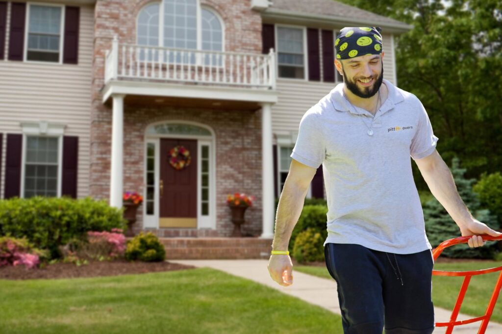 A PittMovers team member pushing a hand truck with a box, walking away from a house in McKees Rocks, PA