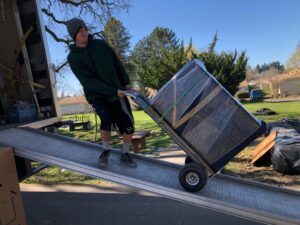 A mover from Emerald Moving & Storage, Inc. pushes a wrapped item up a ramp into a moving truck in Eugene, OR.