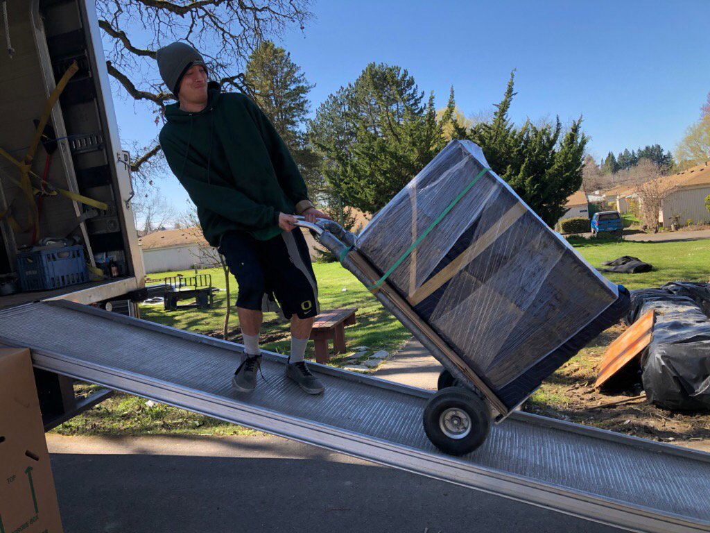 A mover from Emerald Moving & Storage, Inc. pushes a wrapped item up a ramp into a moving truck in Eugene, OR.